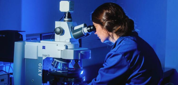 A girl in a lab coat is looking through a microscope